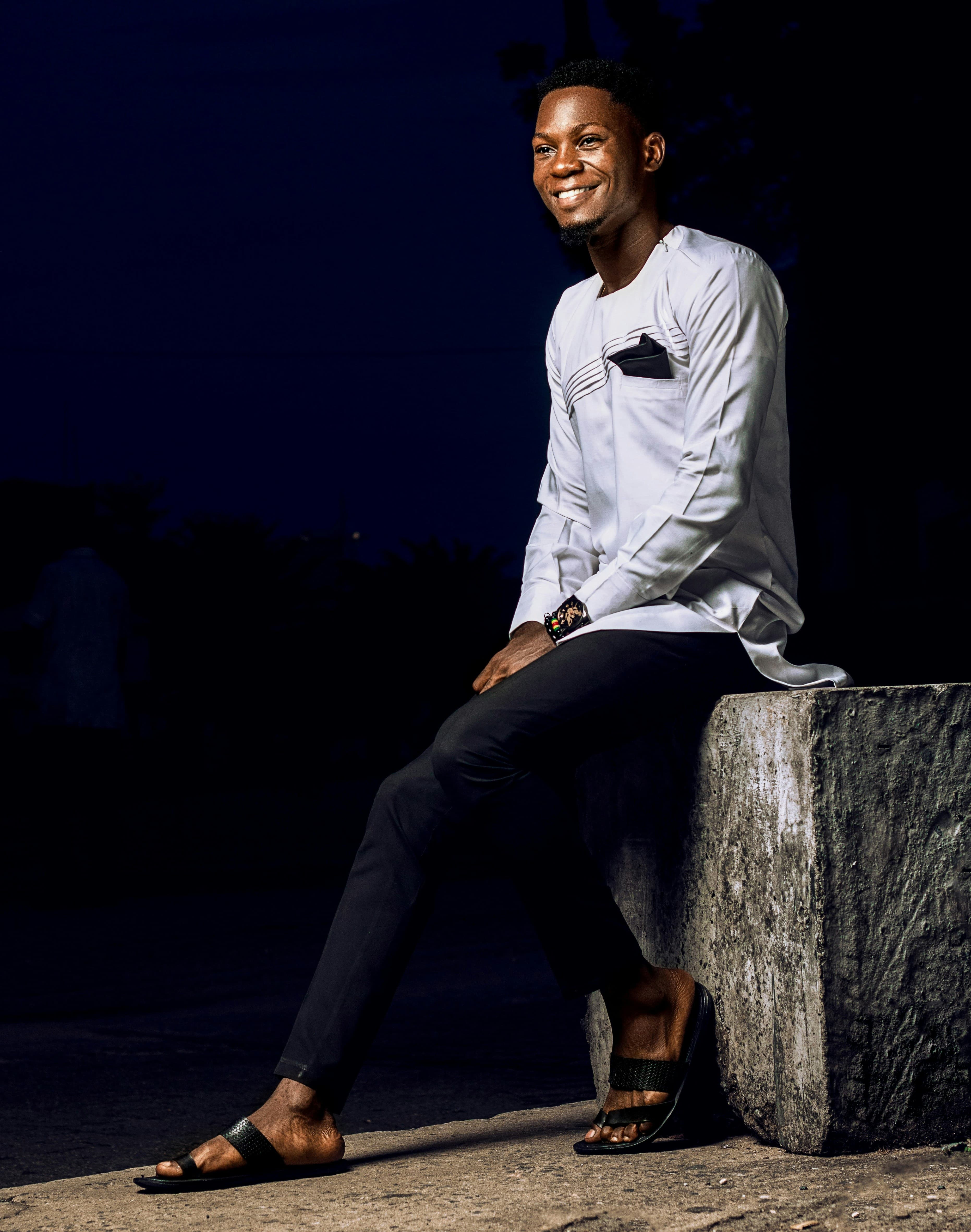 Man in white sitting on a concrete block at night, wearing slides